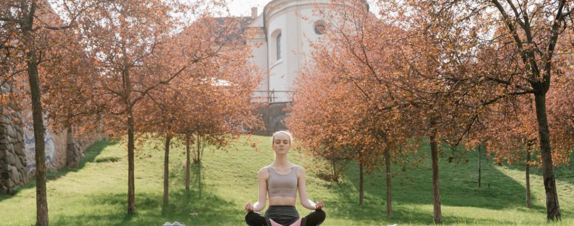 A woman practices meditation outdoors in a tranquil park during fall.